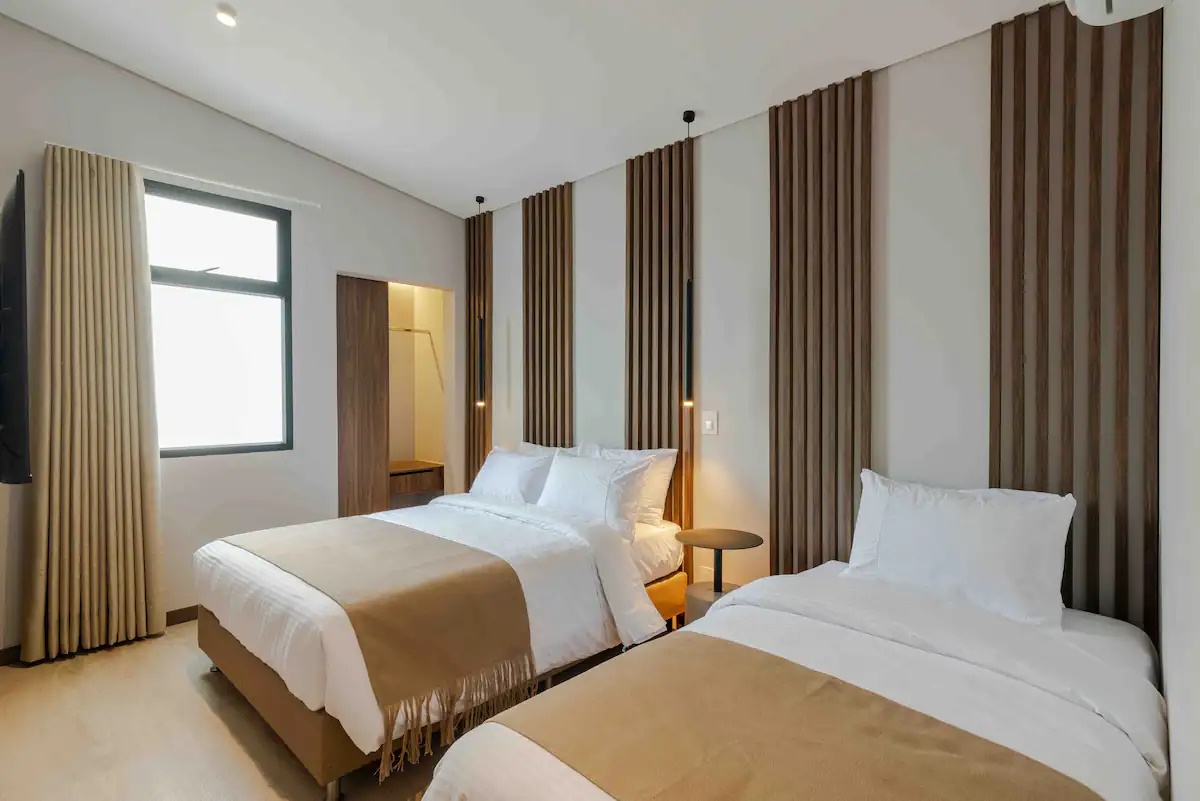 Habitación de apartamento con dos camas, cortinas blackout y acabados en madera